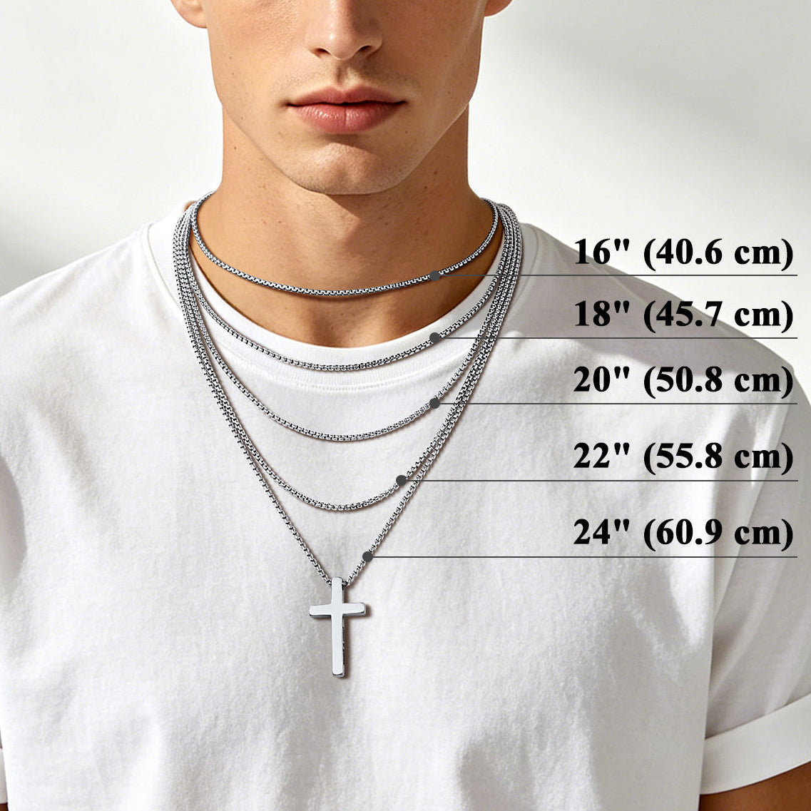 A male model wearing layered silver chain necklaces with a cross pendant, shown against a light neutral background with size measurements listed on the right side for chain lengths from 16 inches to 24 inches.