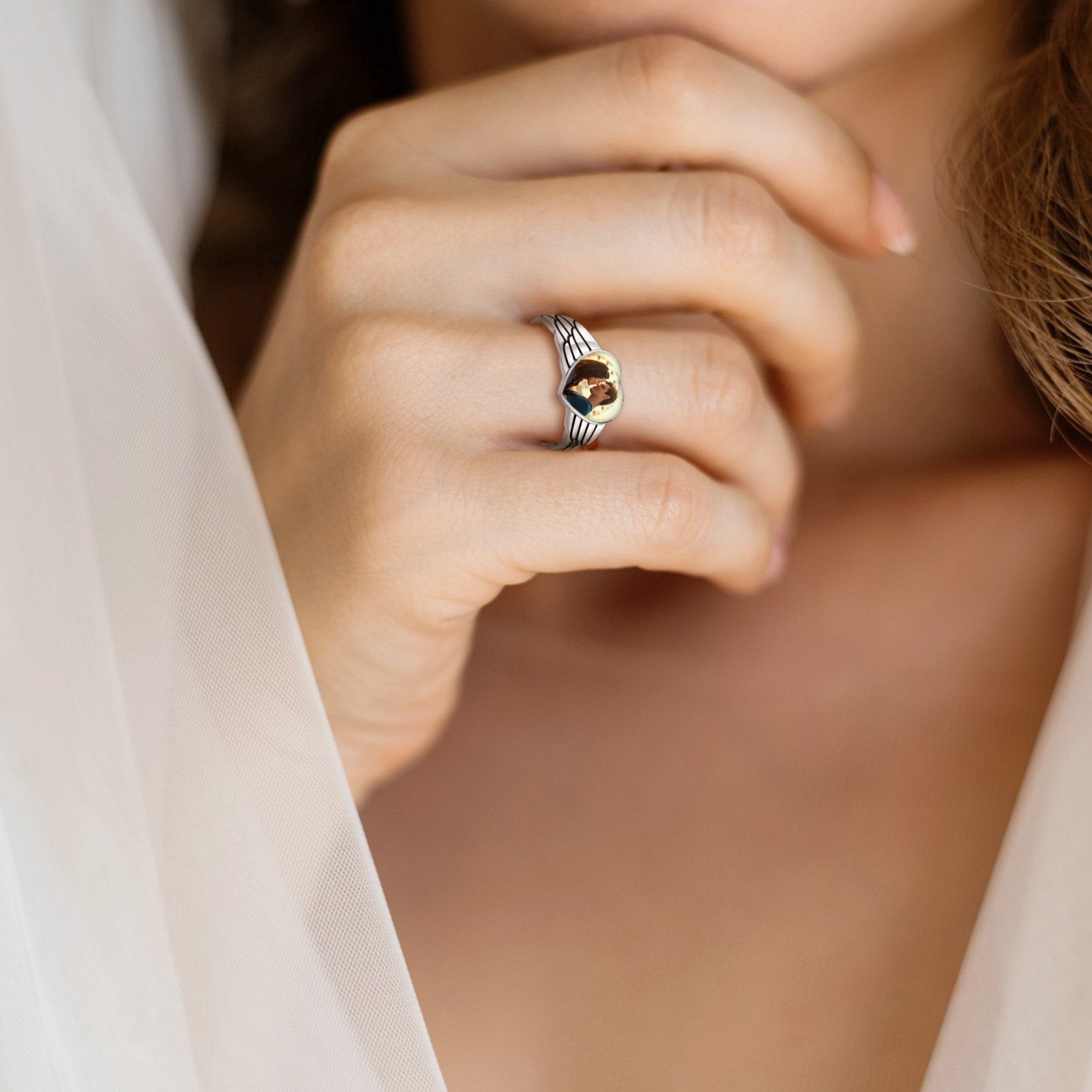 Close-up of a hand wearing a custom heart picture ring with a gemstone, blurred background