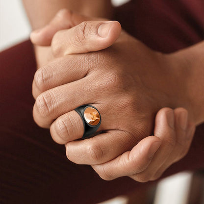Close-up of a hand wearing a custom picture signet ring with a gold center and black band.