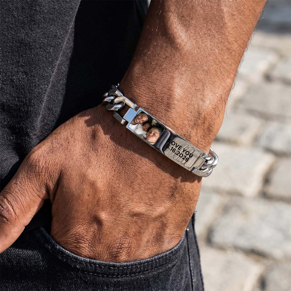 Close-up of a person's wrist wearing a silver chain picutre bracelet with engraved details.