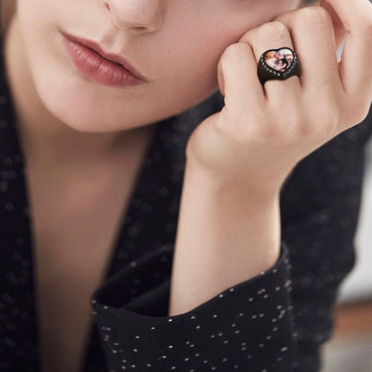 Close-up of a person wearing a black picture signet ring with a heart-shaped design on a blurred background