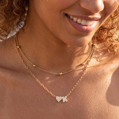 Close-up of a person wearing a gold heart initial necklace with heart-shaped pendants.
