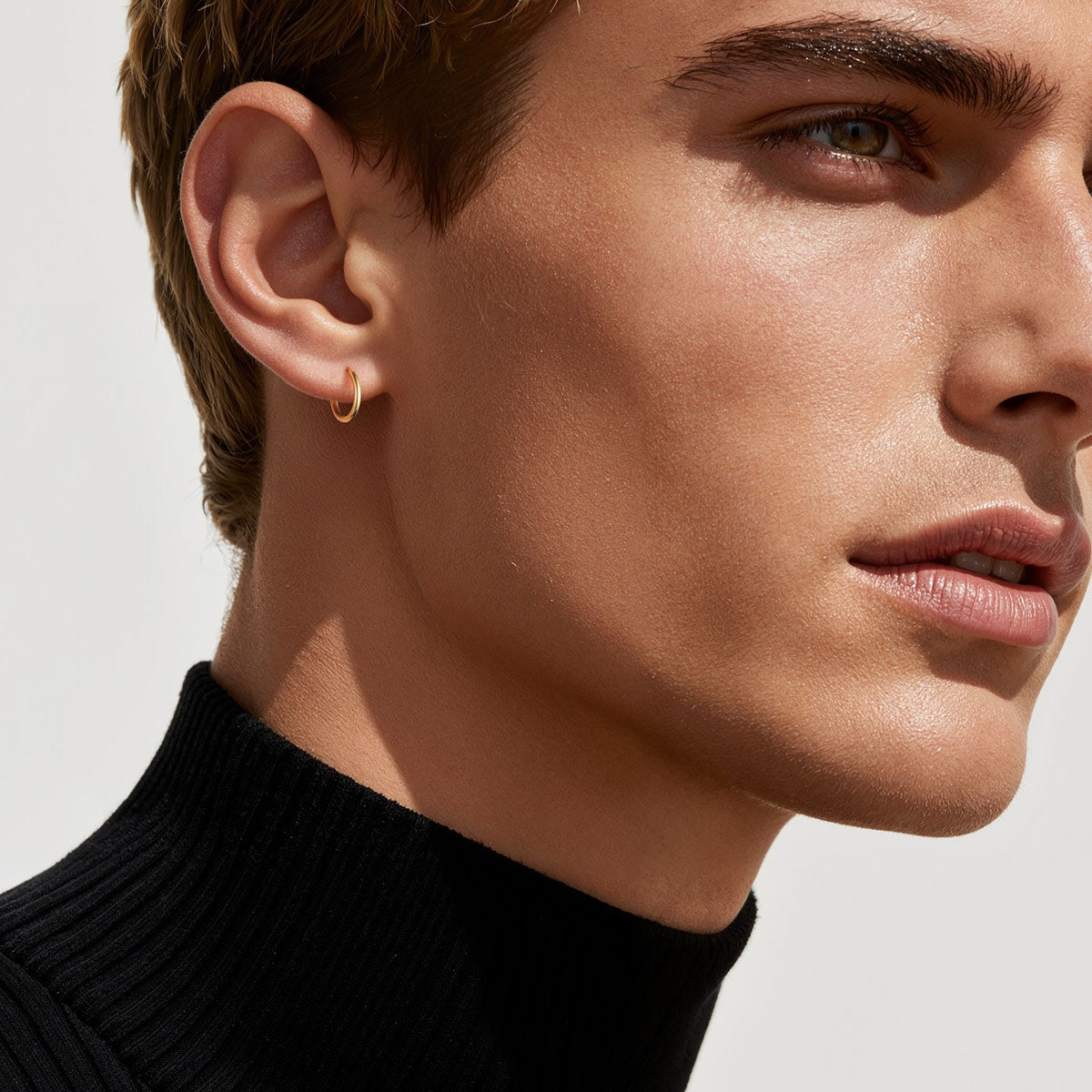 Close-up of a person wearing a gold hoop earring with a neutral background