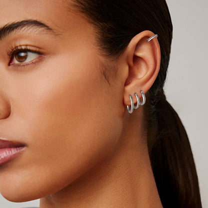 Close-up of a woman's ear wearing a silver huggie earring against a neutral background