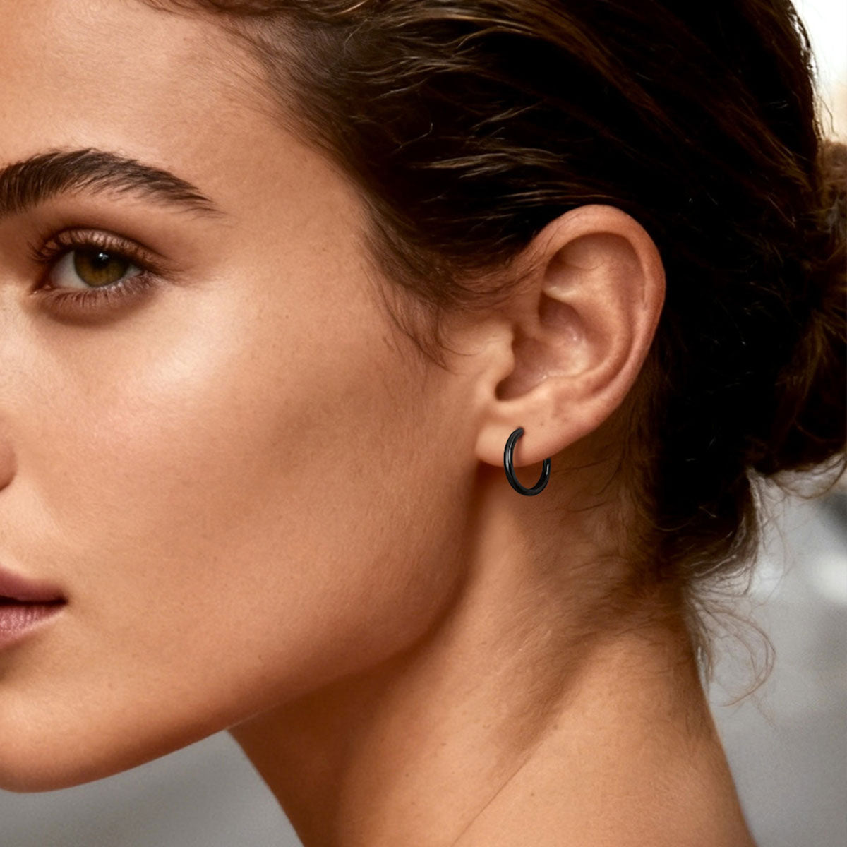 Close-up of a woman's ear with a black hoop earring against a neutral background