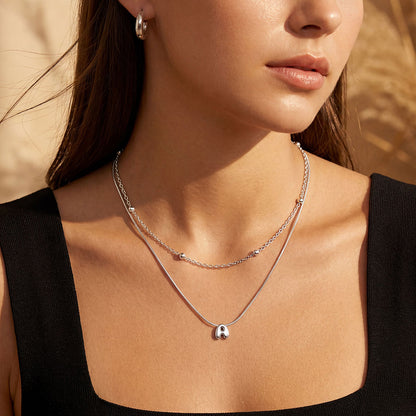 Close-up of a woman wearing a silver bubble initial necklace with a letter 'A' pendant.