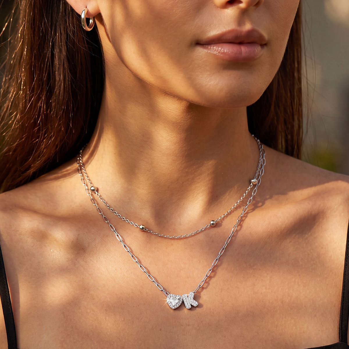 Close-up of a woman wearing a silver layered initial necklace with a heart and letter pendant.
