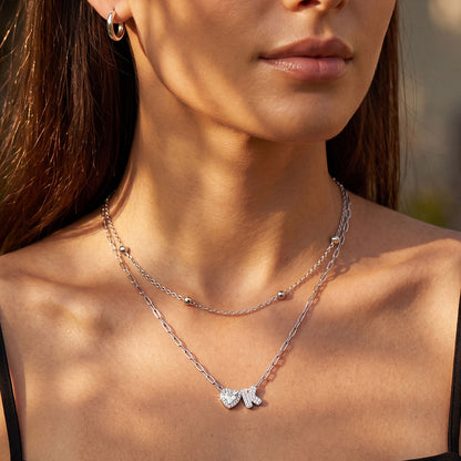 Close-up of a woman wearing a silver layered initial necklace with a heart and letter pendant.