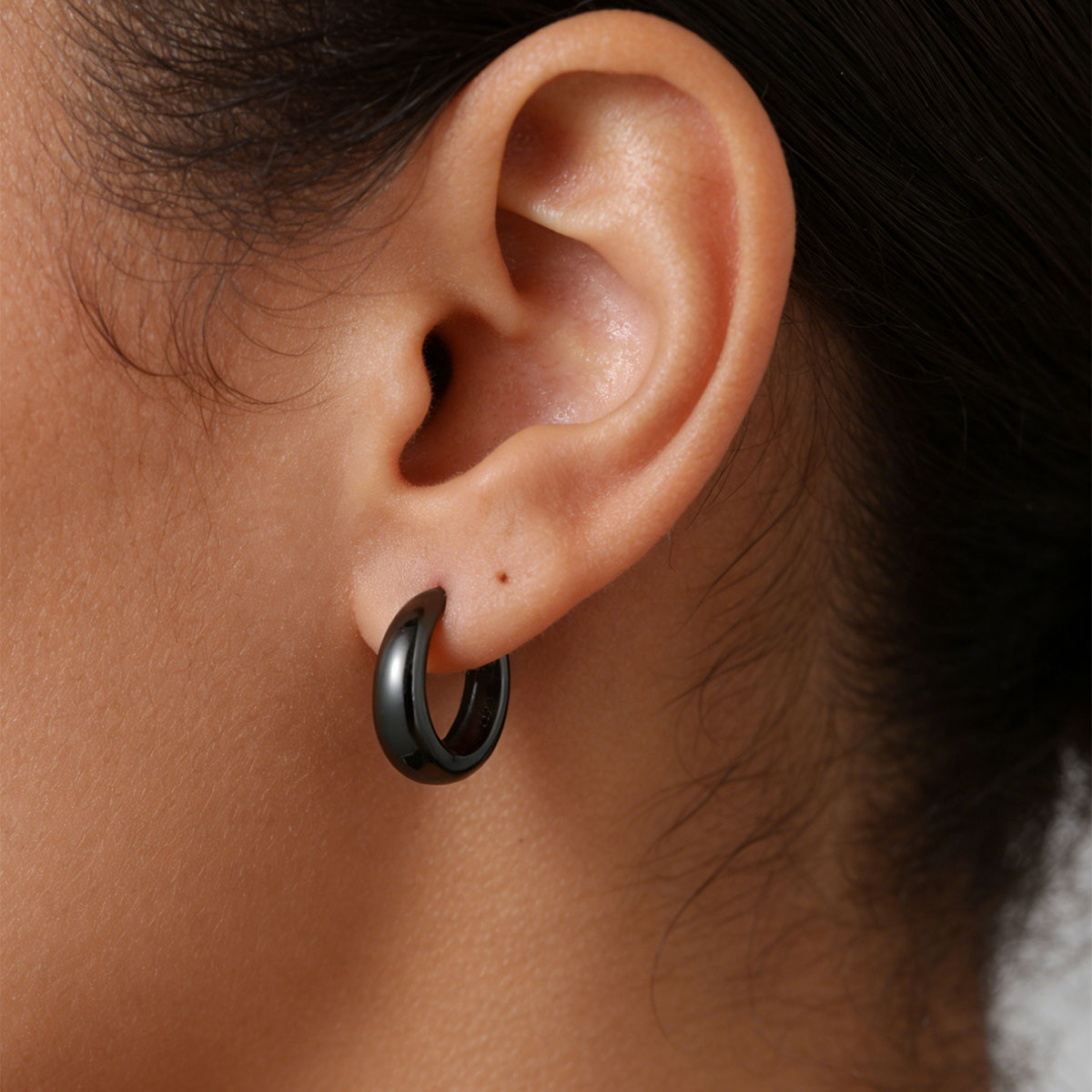 Close-up of an ear wearing a black huggie earring with blurred background