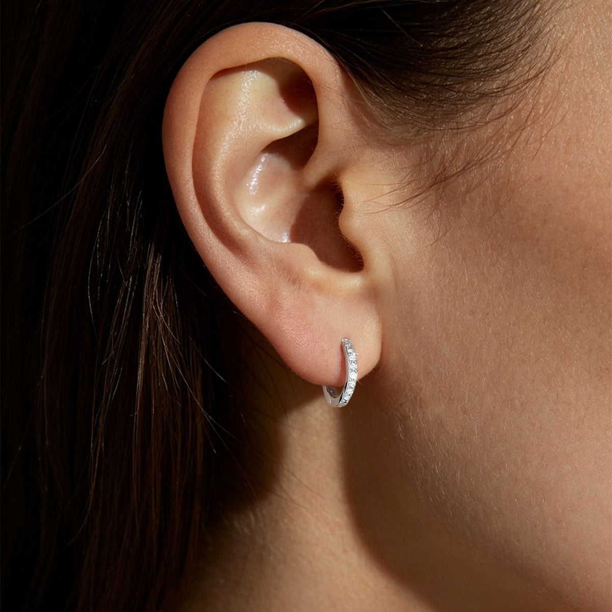 Close-up of an ear wearing a cz silver huggie earring with a dark background