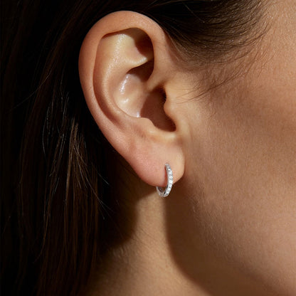 Close-up of an ear wearing a cz silver huggie earring with a dark background