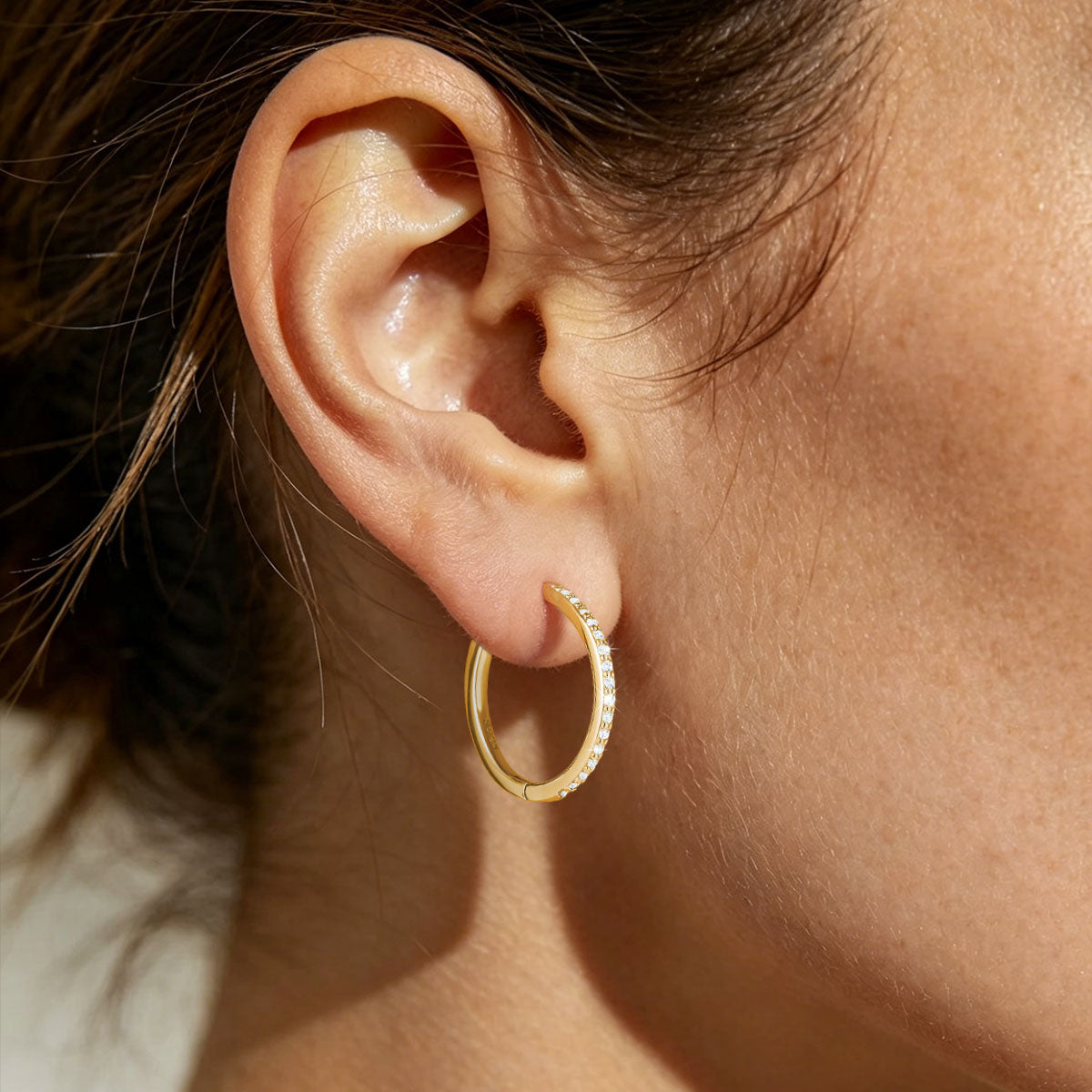Close-up of an ear wearing a gold cz huggie earring 