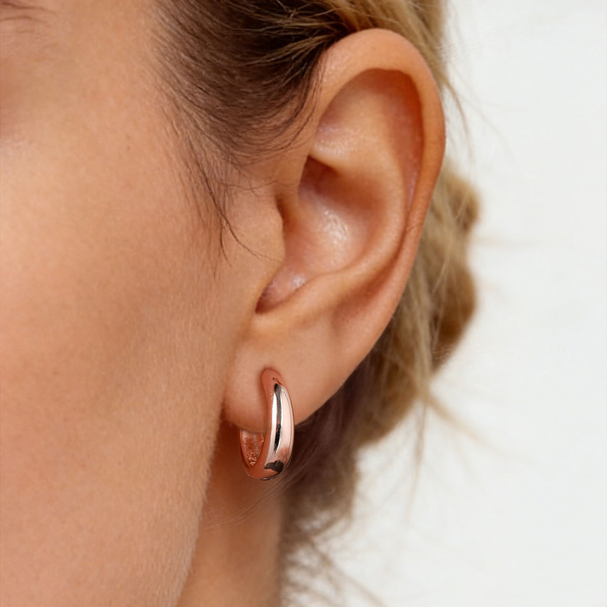 Close-up of an ear wearing a rose gold huggie earring on a neutral background