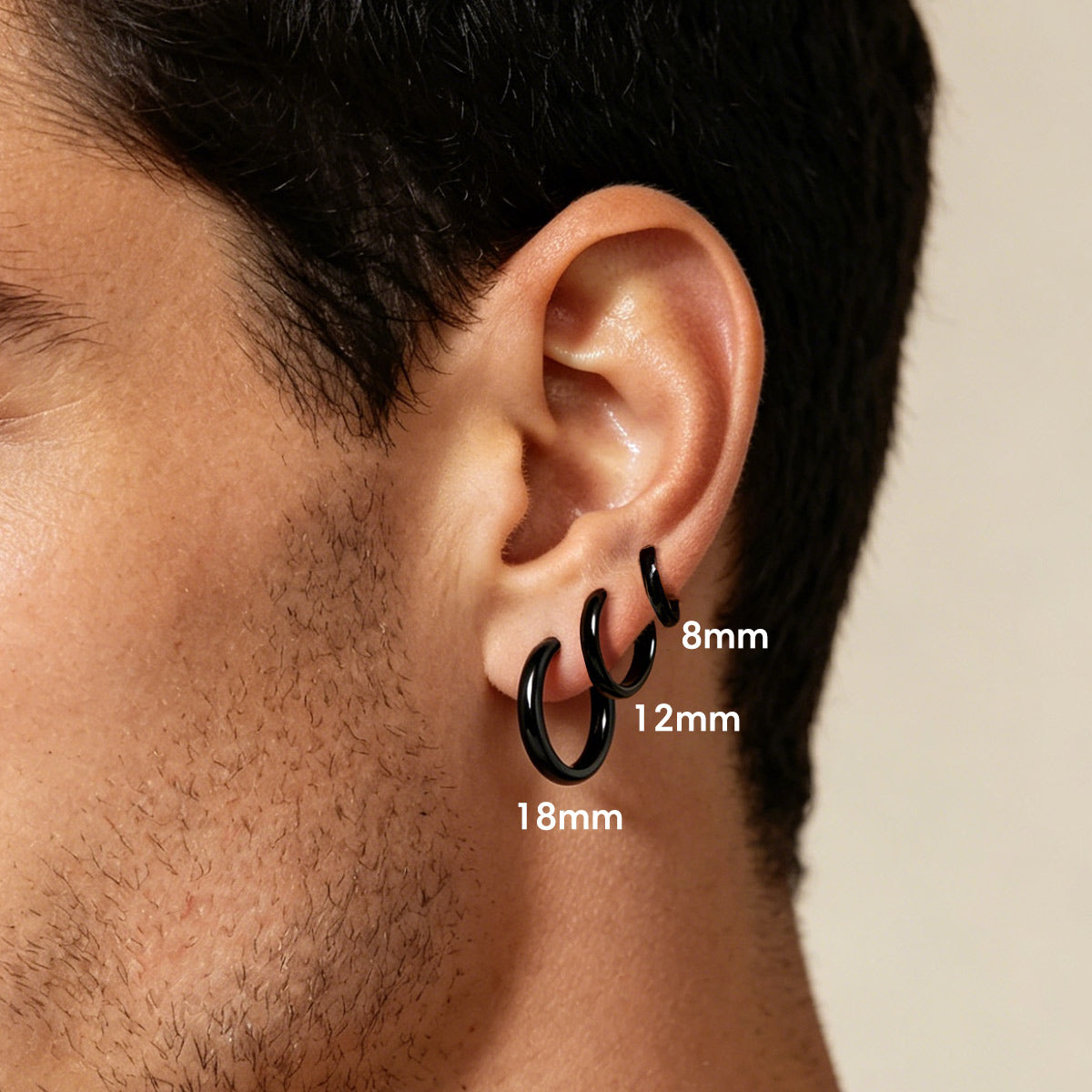 Close-up of an ear wearing black huggie earrings with size labels.