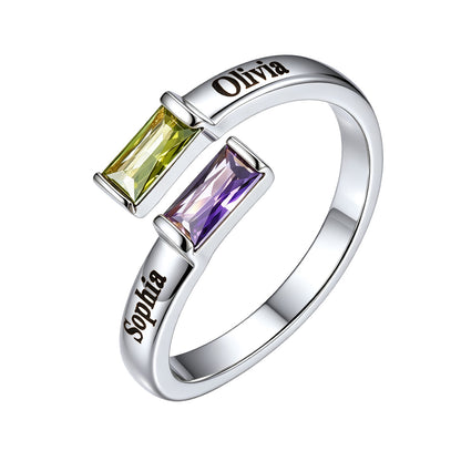 A silver ring featuring two baguette gemstones, one yellow-green and one purple, with the names 'Olivia' and 'Sophia' engraved on the polished band, set against a plain white background.