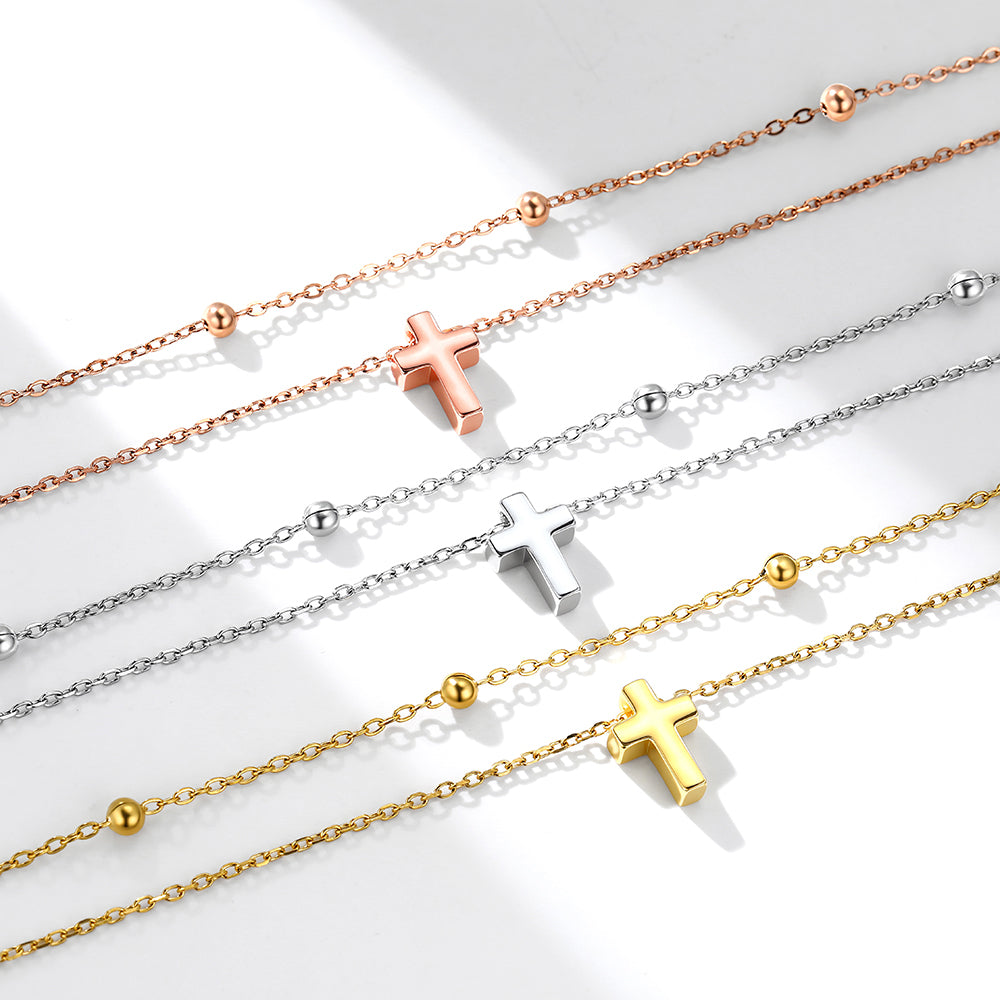Four necklaces with cross pendants in rose gold, silver, and gold on a light background