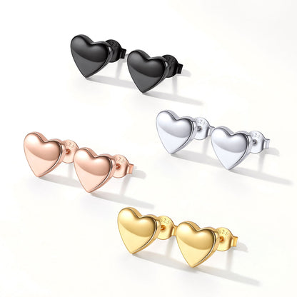 Four pairs of heart-shaped stud earrings arranged on a clean white background, shown in black, rose gold, silver, and yellow gold finishes.