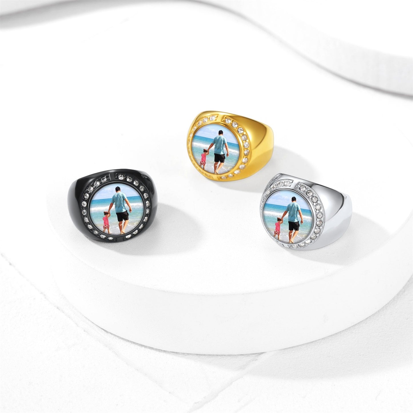 Four rings in black, gold, silver, and white with family beach scene engraving on a white background