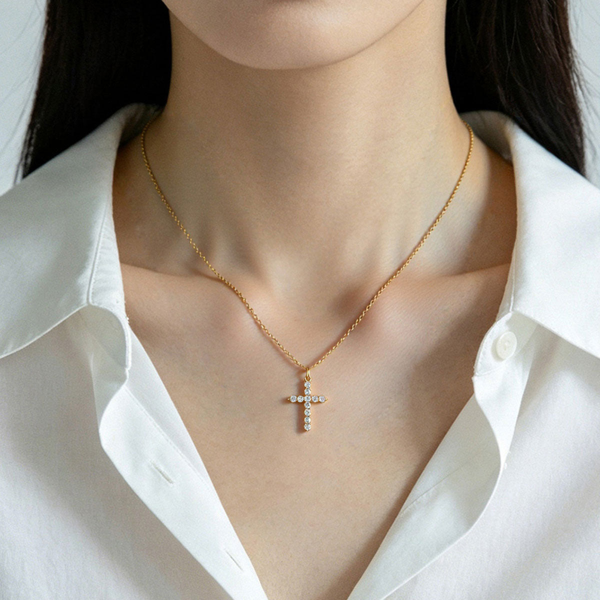 Gold CZ cross necklace worn by a person in a white shirt