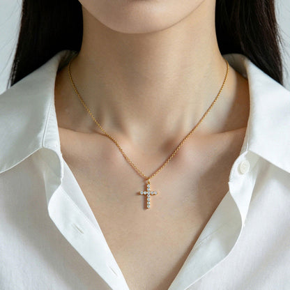 Gold CZ cross necklace worn by a person in a white shirt