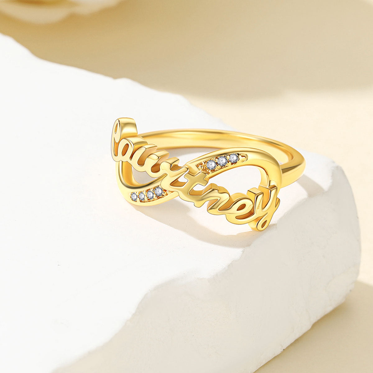 Gold Custom Name Infinity Promise Ring With Cubic Zirconia ion a light yellow background