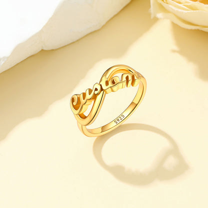 Gold Plated Custom Name Infinity Promise Ring for Women on white stone on a light yellow backgound
