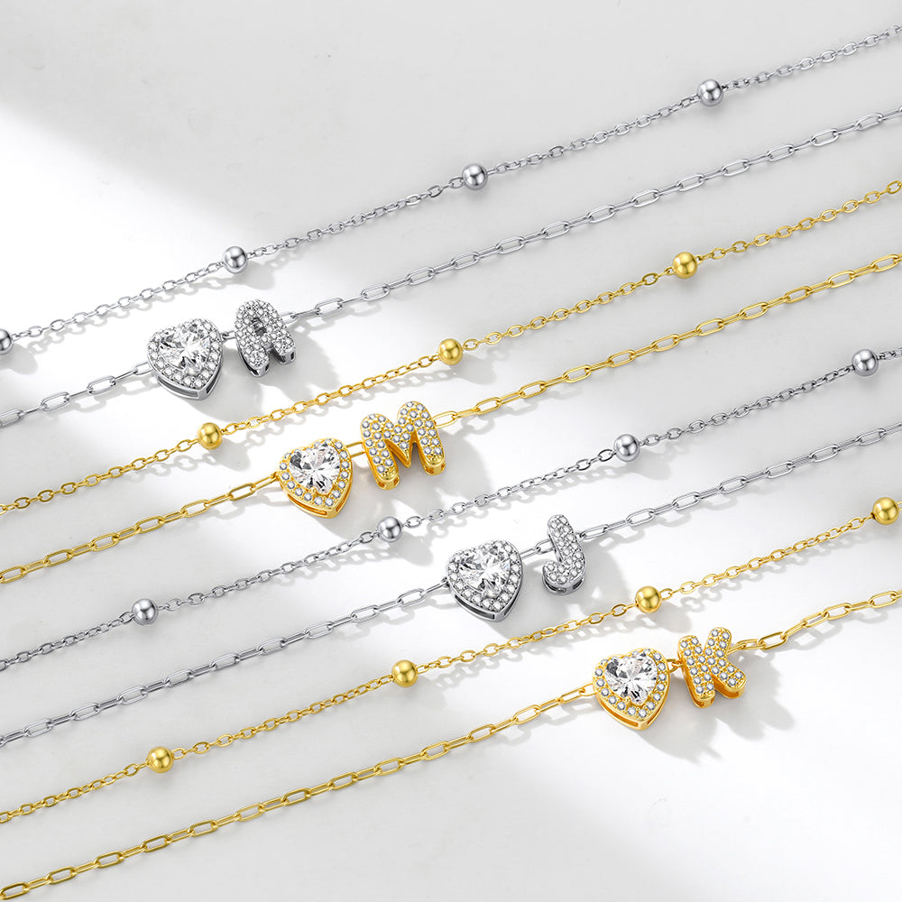 Gold and silver initial necklaces with heart and bow pendants on a light background