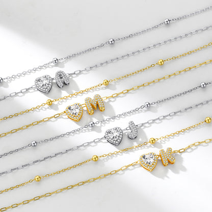 Gold and silver initial necklaces with heart and bow pendants on a light background