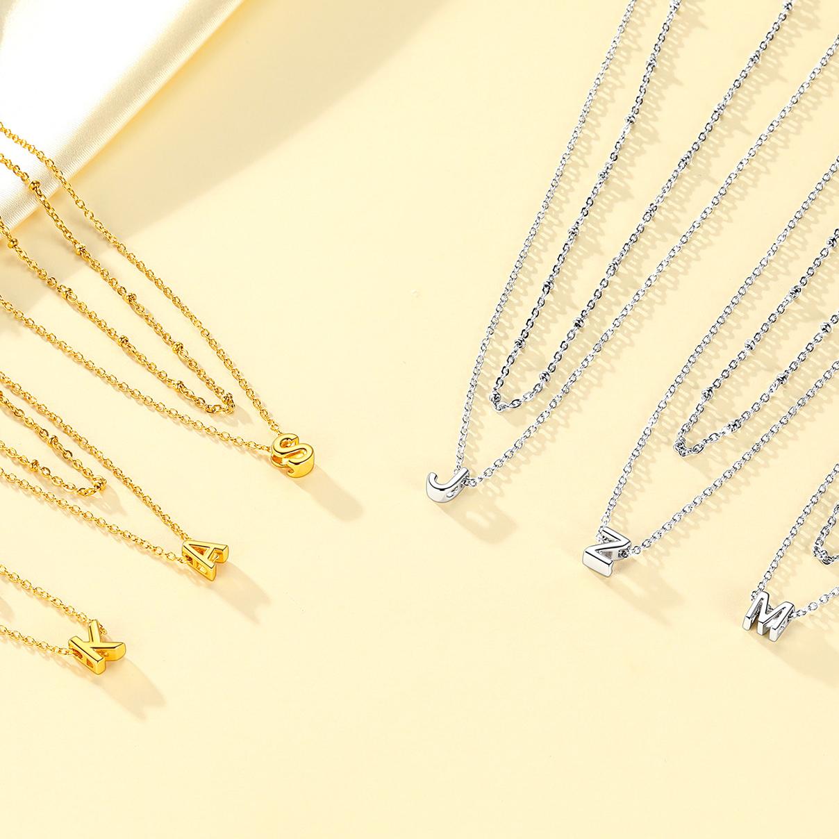 Gold and silver initial necklaces with letter pendants on a light yellow background