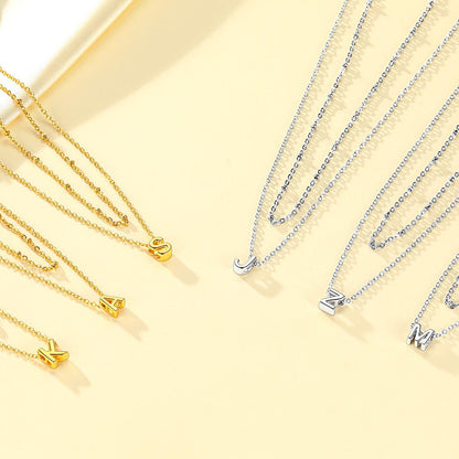 Gold and silver initial necklaces with letter pendants on a light yellow background
