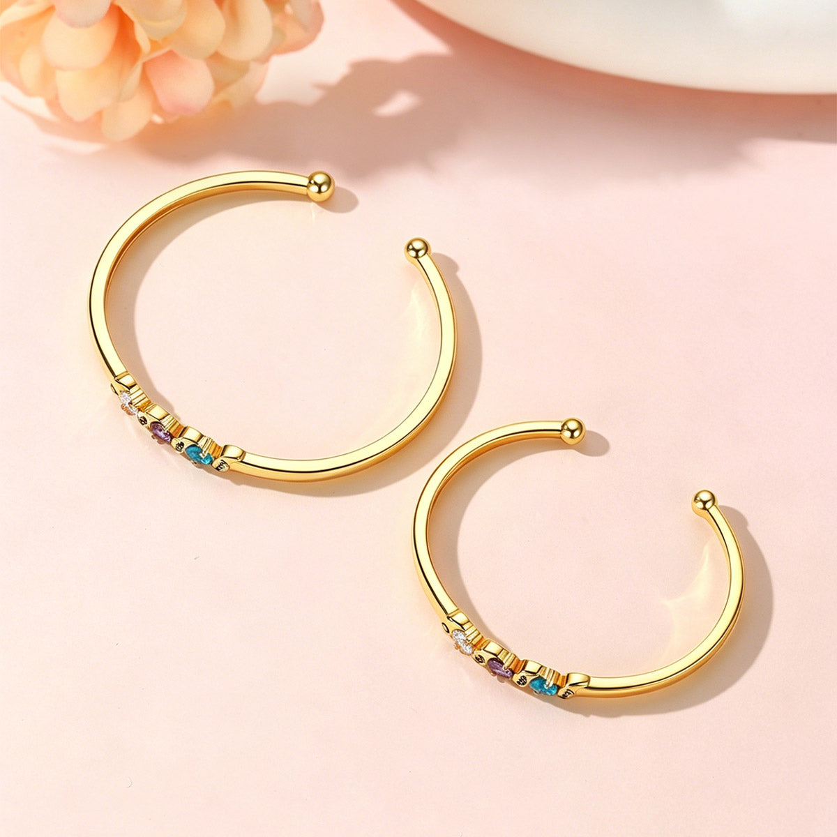 Gold birthstone cuff bracelet in different size with colorful beads on a pink background