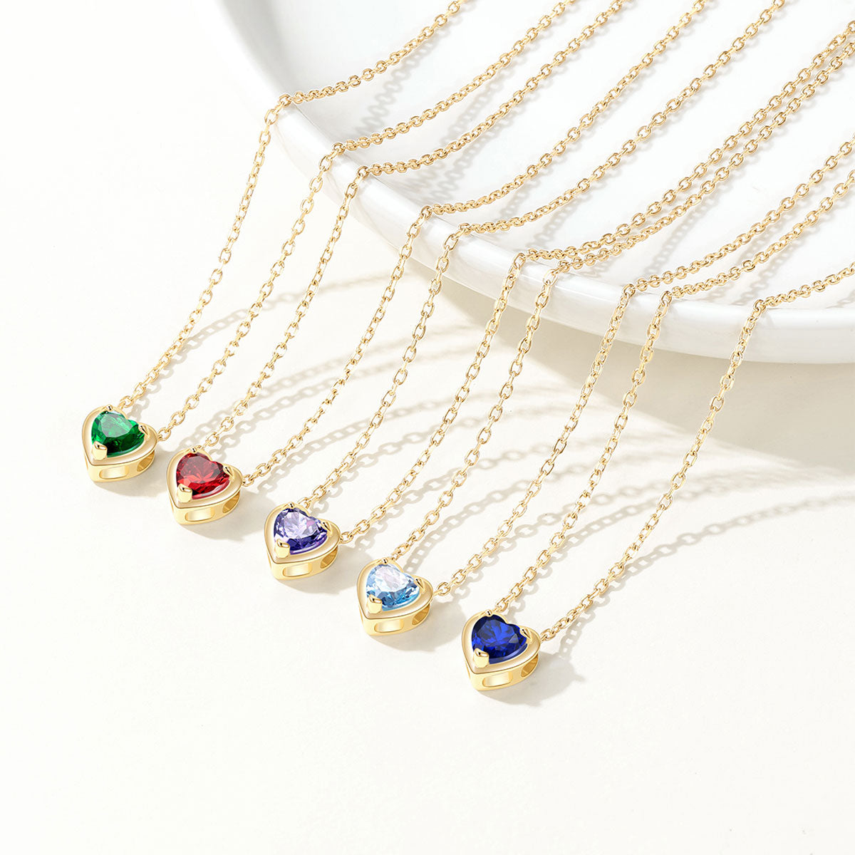Gold birthtsone necklaces with heart-shaped gemstones on a white background