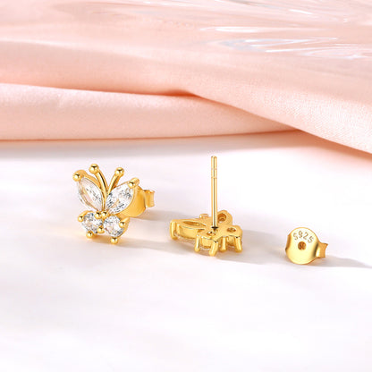 Gold butterfly stud earrings with clear gemstones, shown with one earring facing forward, one showing the back post, and a separate round back clip on a white surface with a soft pink satin background.