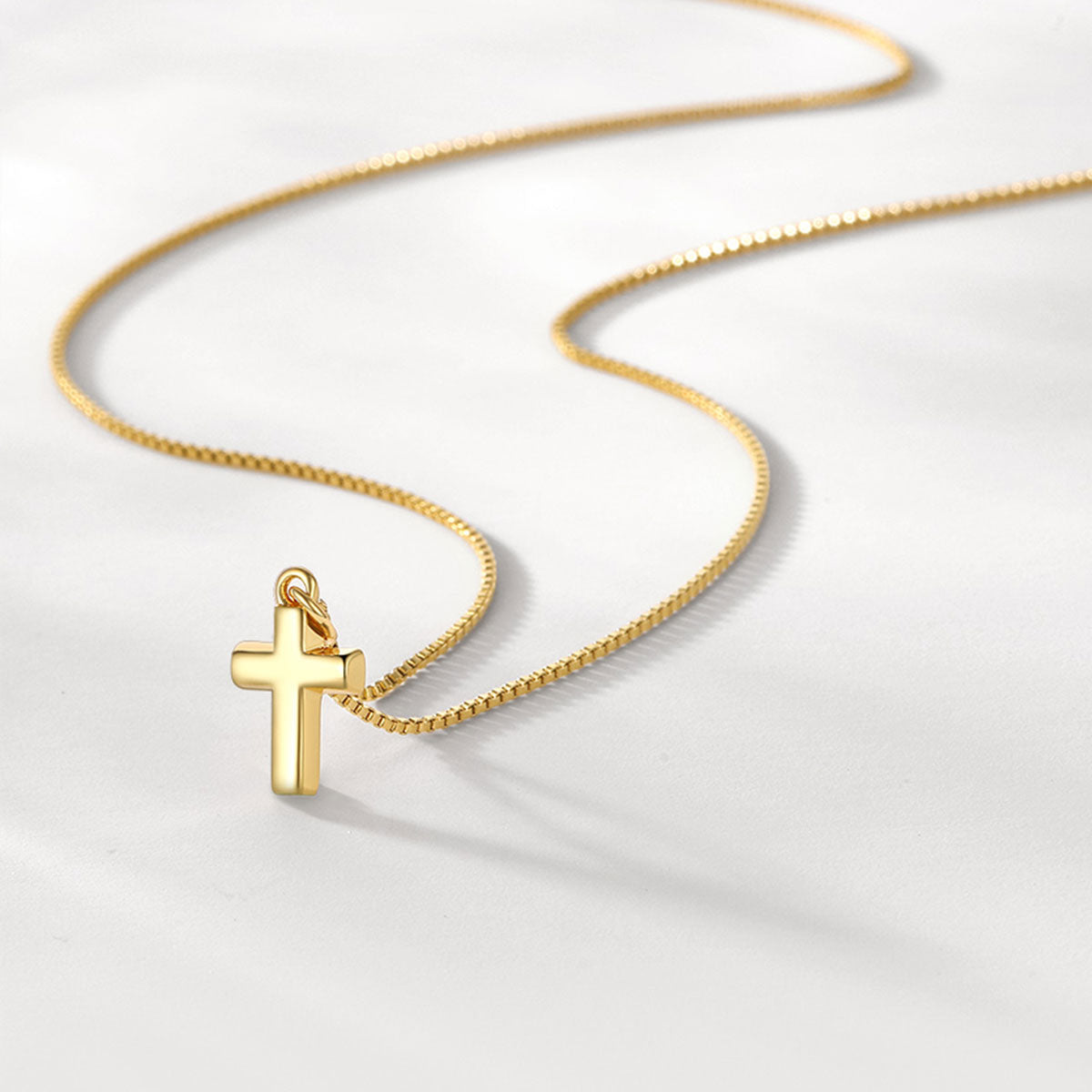 Gold cross necklace on a light gray background