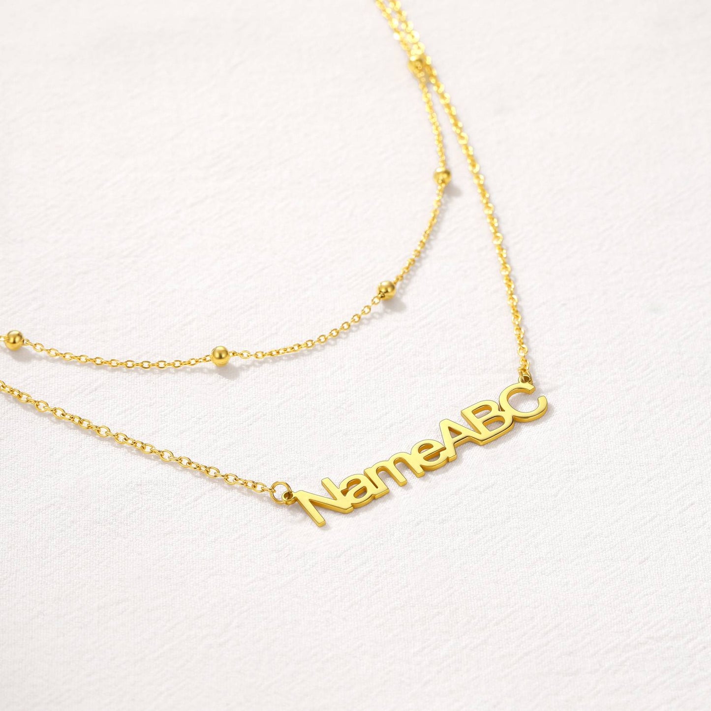 Gold custom name necklace with 'NameABC' pendant on a light gray background