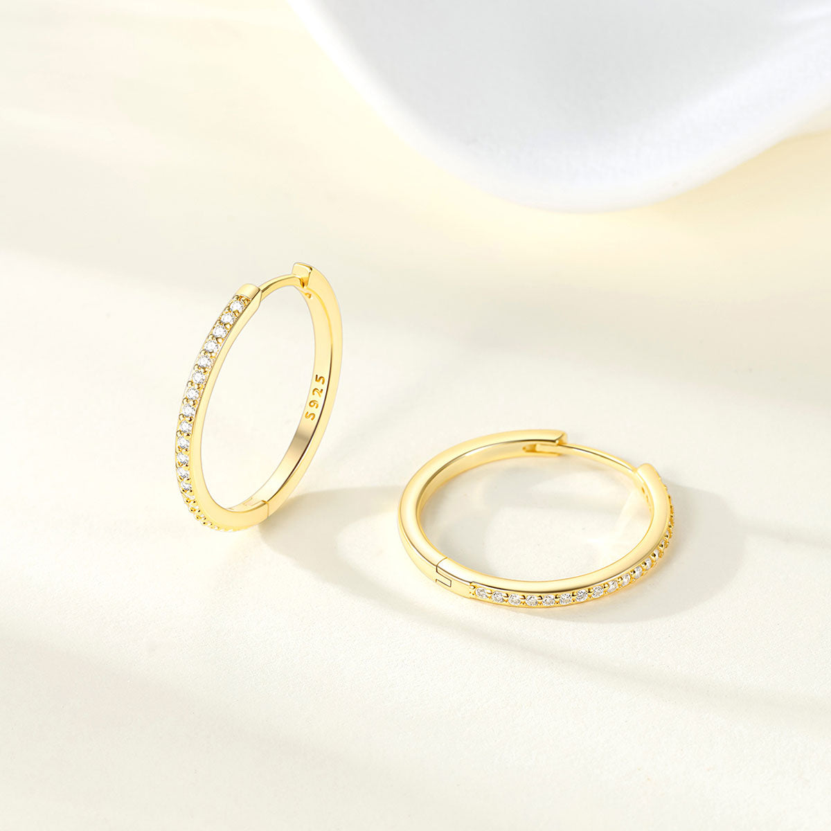 Gold huggie earrings with embedded cz on a light background