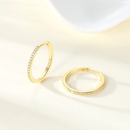 Gold huggie earrings with embedded cz on a light background