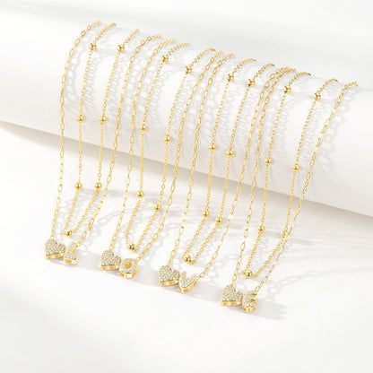 Gold initial necklaces with heart-shaped pendants on a white background