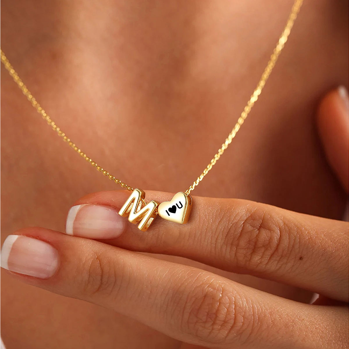 Gold necklace with 'M I ❤️ U' charms on a person's hand.