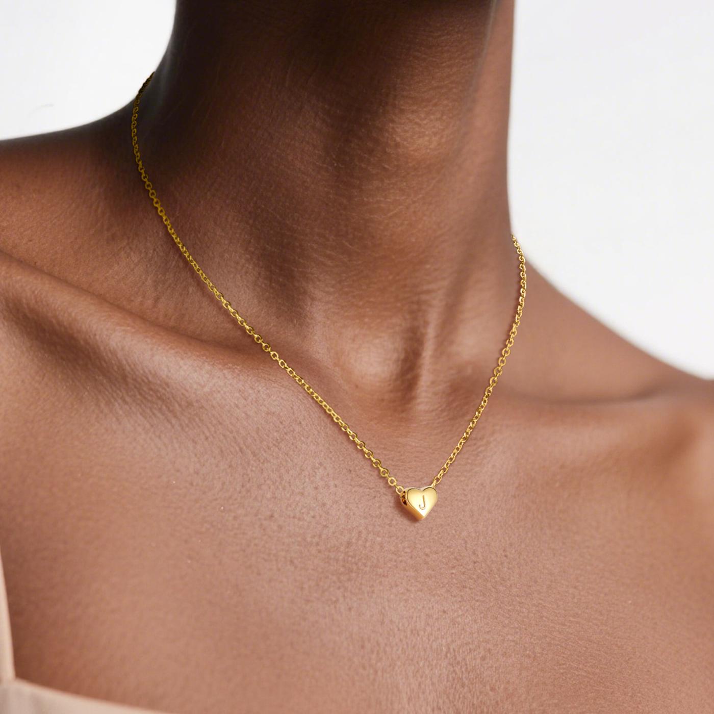 Gold necklace with a heart pendant on a person's neck against a neutral background