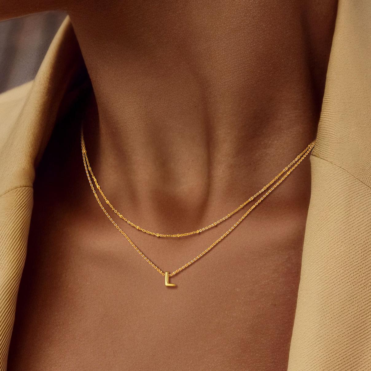 Gold necklace with a letter 'L' pendant on a person wearing a beige coat.