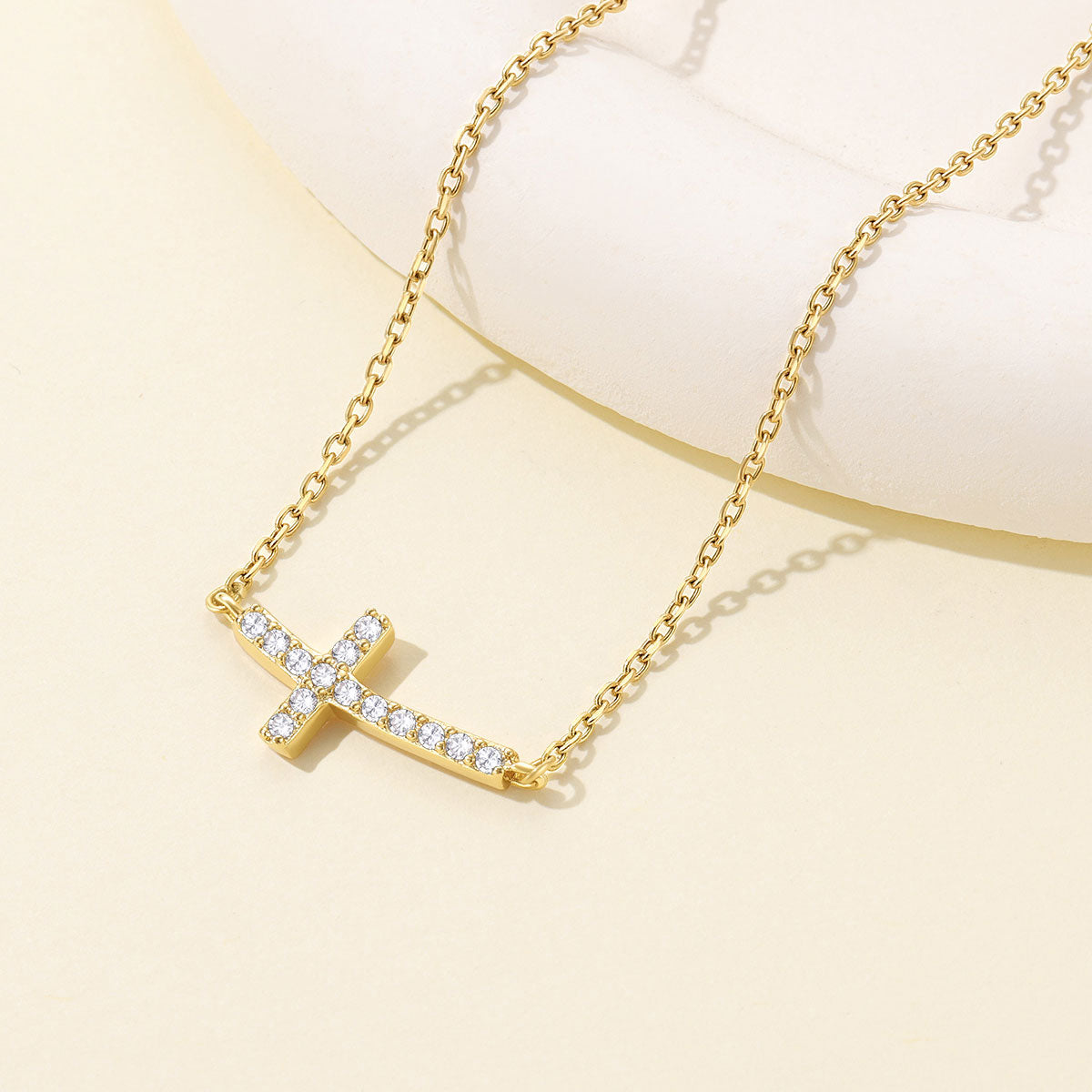 Gold plated Dainty Cubic Zirconia Sideways Cross Necklace for Women on a light yellow background