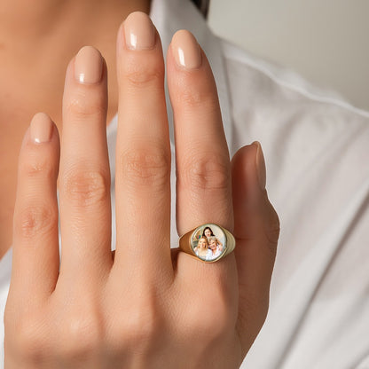 Gold ring with a custom picture signet ring on a person's hand against a neutral background