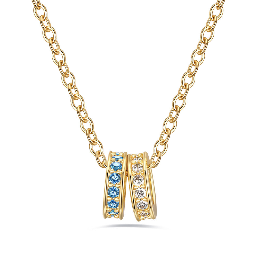 Gold stacking birrthstone necklace with two ring pendants featuring blue and clear stones on a white background