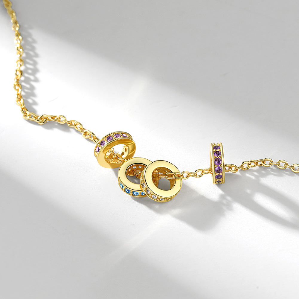 Gold stacking birthstone necklace with circular pendants and embedded gemstones on a light gray background