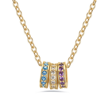 Gold stacking birthstone necklace with three interlocking rings each containing different colored gemstones on a white background