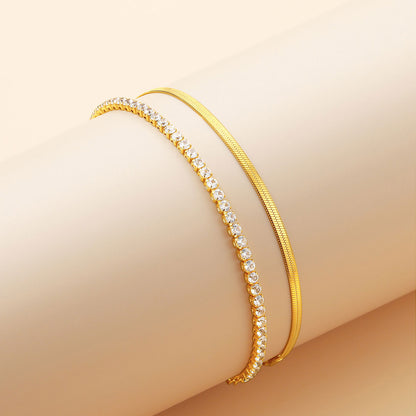 Gold tennis and herringbone ankle bracelet set with small diamonds on a beige background