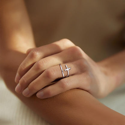 Hand wearing a silver cross ring on a blurred background