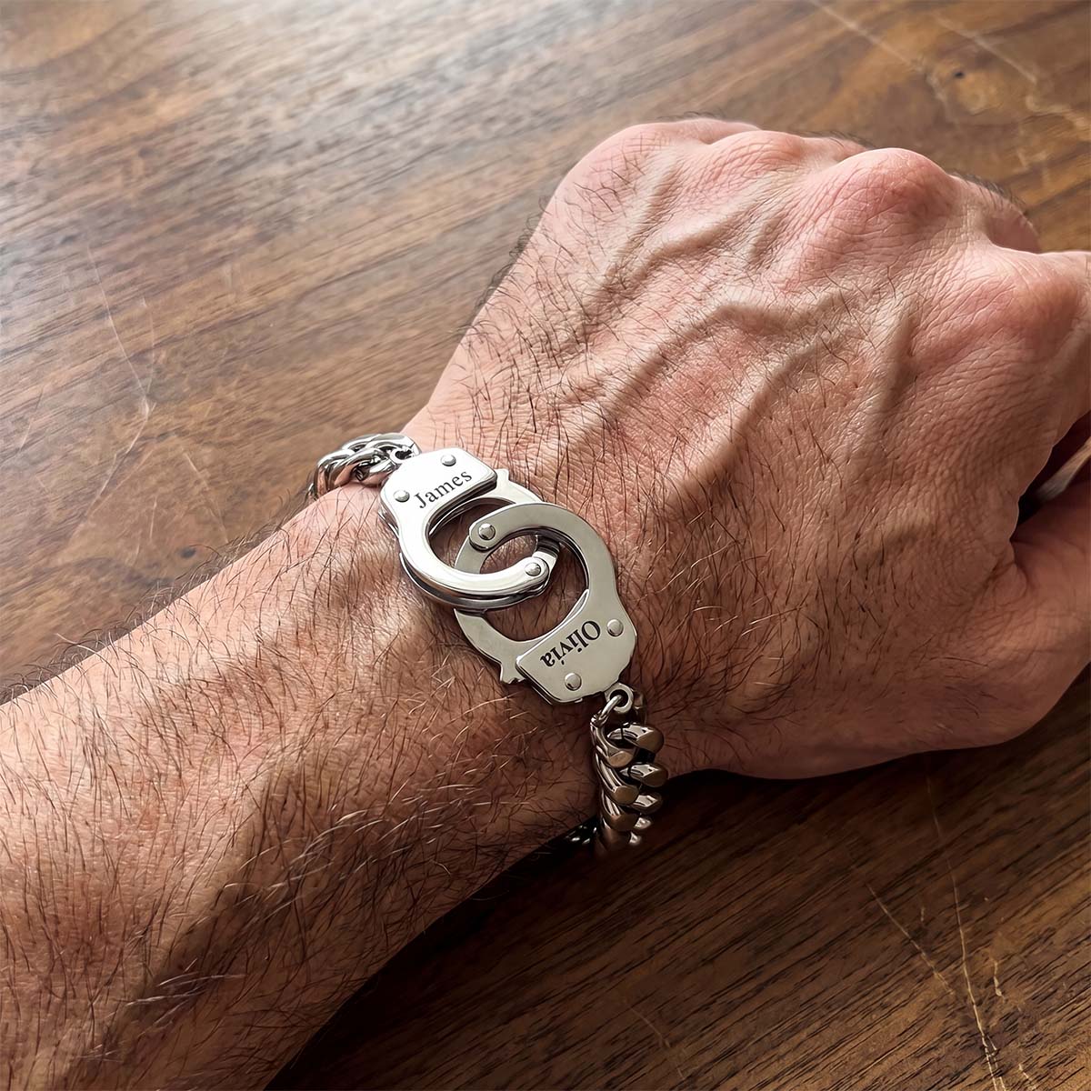 Hand wearing a silver custom handcuff bracelet on a wooden surface