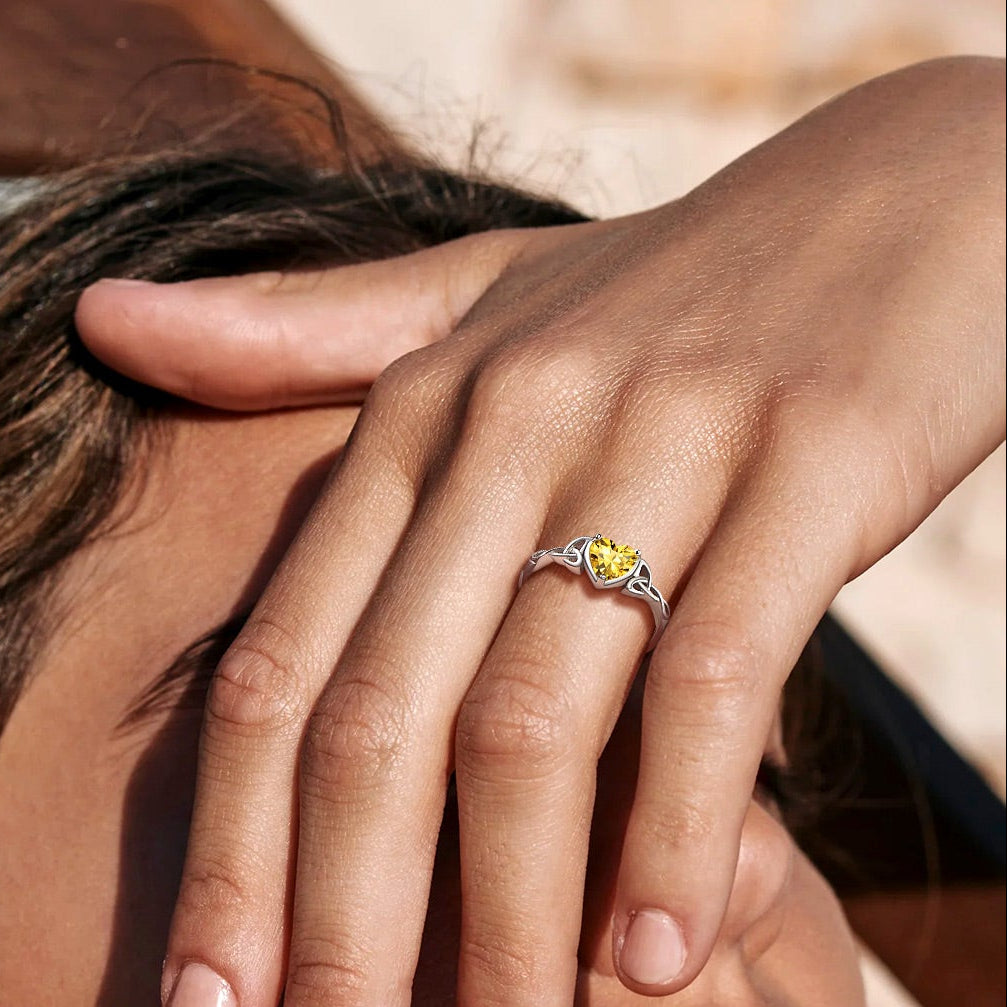 Close-up of a woman's face with a hand covering her eye, wearing a ring with a yellow gemstone.